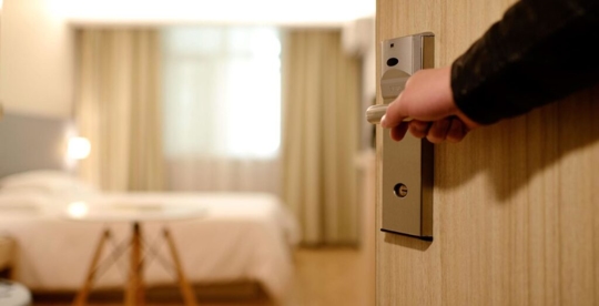 hand on a door handle opening up a door to a hotel room